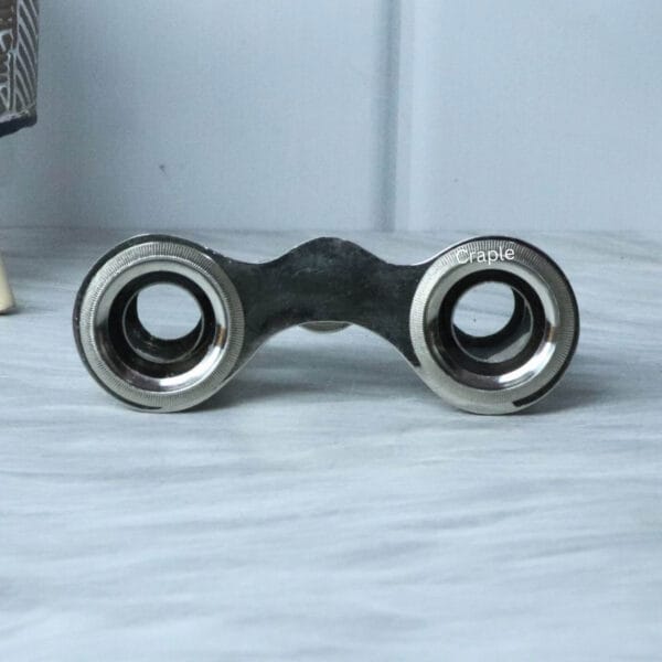 Close-up view of the eyepieces on a pair of nickel-plated antique pocket binoculars, showing the lens and frame.