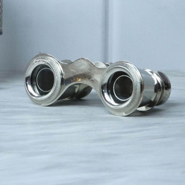 Angled side profile of vintage-style nickel-finish opera glasses resting on a marble surface.