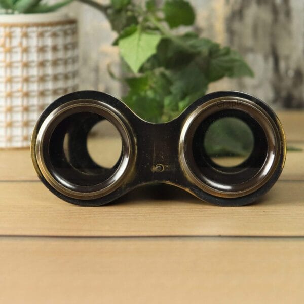 Top-down view of antique black engraved brass binoculars, showing the dark finish of the eyepieces and bridge.