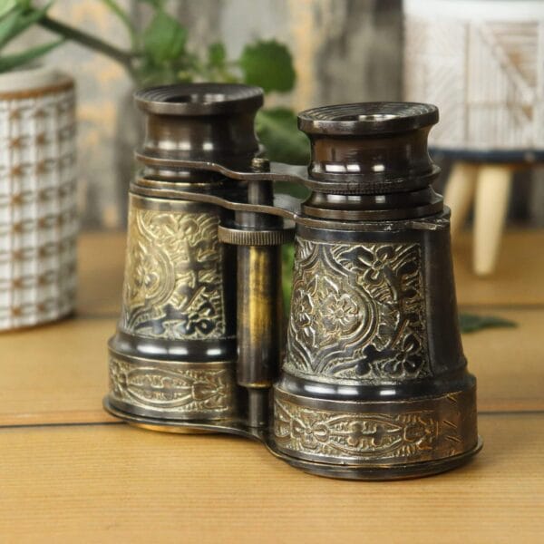 Side view of collectible engraved brass opera glasses with a focus knob, showing the black antique patina.