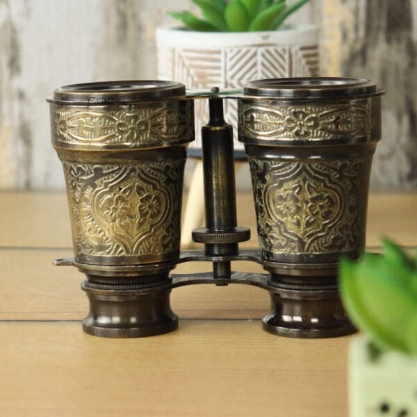 Detailed close-up of the floral engraving on the brass barrels of the antique-style binoculars.