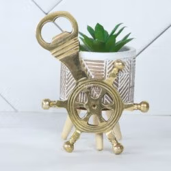 The brass ship's helm bottle opener displayed as a stylish decorative piece next to a small potted plant.