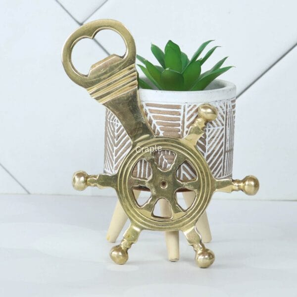 The brass ship's helm bottle opener displayed as a stylish decorative piece next to a small potted plant.