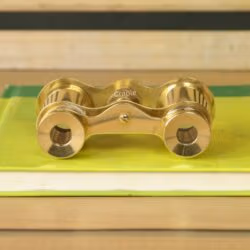 Top-down view of vintage brass opera glasses on a book, showing the bridge, knurled focus knob, and eyepiece design.