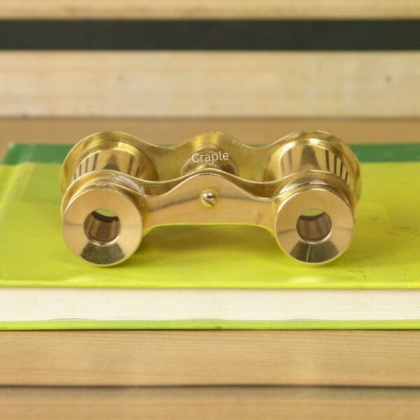 Shiny Brass Decorative Binoculars-1 Top-down view of vintage brass opera glasses on a book, showing the bridge, knurled focus knob, and eyepiece design.