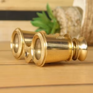 Detailed close-up side view of antique-style brass binoculars, highlighting the shiny finish on the eyepieces and barrels.