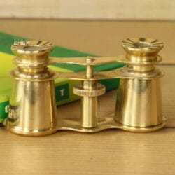 Front view of compact Victorian-style brass theater binoculars with 2X magnification, resting on a green book.
