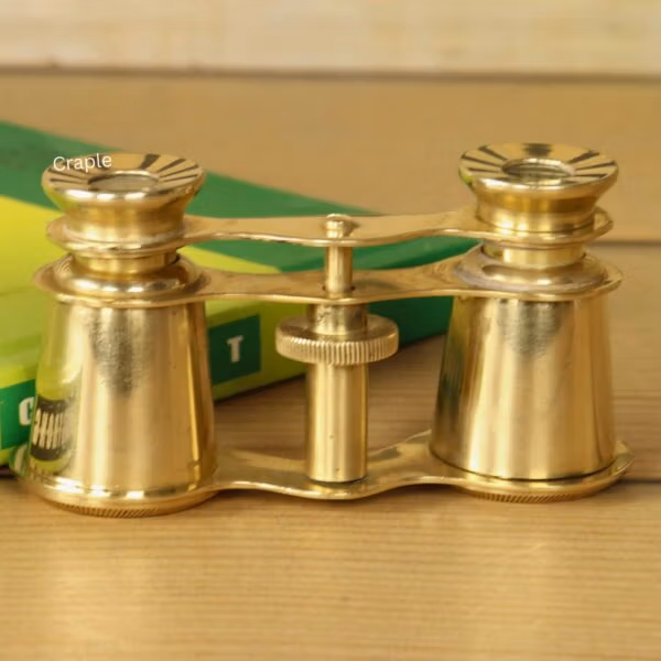 Front view of compact Victorian-style brass theater binoculars with 2X magnification, resting on a green book.