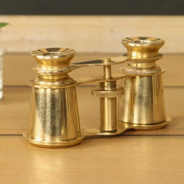 Angled front view of vintage solid brass opera glasses with a central focus wheel, sitting on a wooden surface.