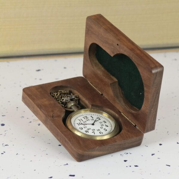 The antique brass pocket watch presented in an open dark wood gift box with a green velvet lining.