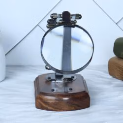 Front view of a vintage folding desk magnifier in its compact, folded position on a polished wood base.