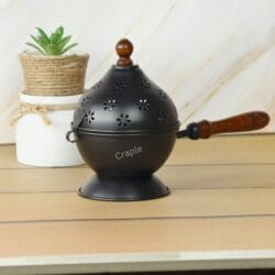 Black iron Loban Dani incense burner with a wooden handle, displayed as a stylish piece of home decor next to a plant.
