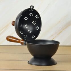 Open view of the black iron charcoal incense burner, with the floral perforated lid placed next to the deep bowl.