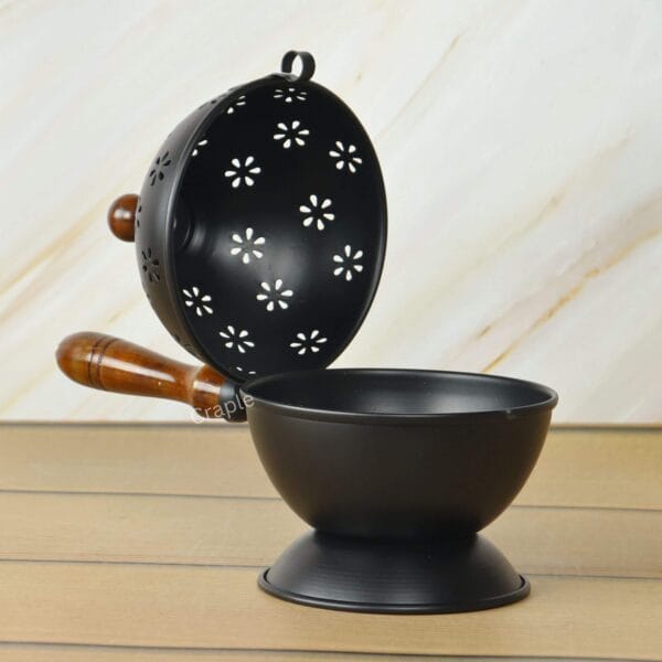 Open view of the black iron charcoal incense burner, with the floral perforated lid placed next to the deep bowl.