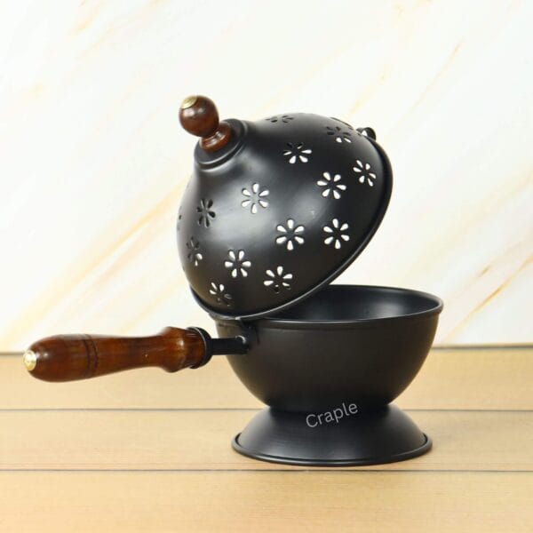 Black iron incense burner (Loban Dani) with its perforated floral-pattern lid hinged open, showcasing the bowl and wooden handle.