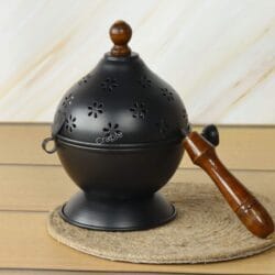 The traditional black iron incense burner shown on a coaster with a pair of tongs, ready for use with charcoal.