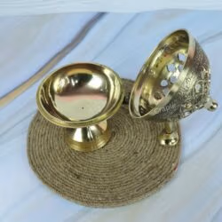 The brass charcoal incense burner shown in two pieces, with the decorative lid resting next to the pedestal base.