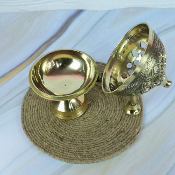 The brass charcoal incense burner shown in two pieces, with the decorative lid resting next to the pedestal base.