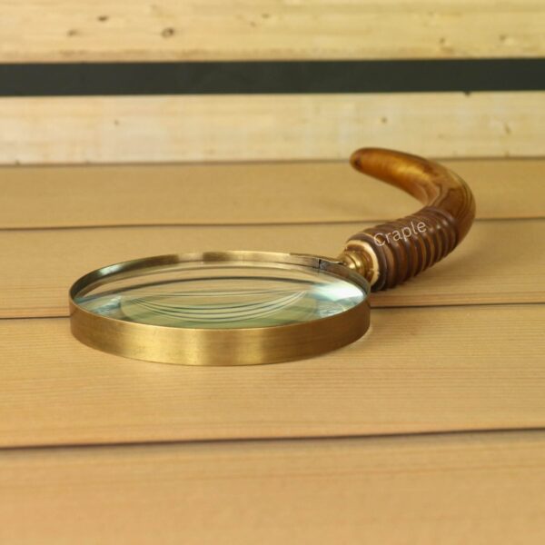 Side profile of a vintage magnifying glass with an antique brass rim and a curved wooden handle with a ribbed grip.