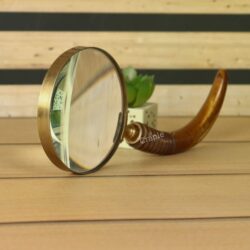 An antique-style brass magnifier standing on its edge, reflecting light and showing the quality of the glass.
