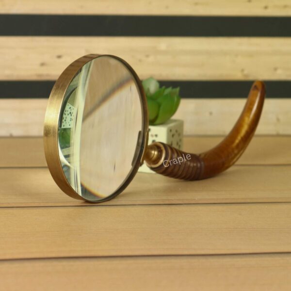 An antique-style brass magnifier standing on its edge, reflecting light and showing the quality of the glass.