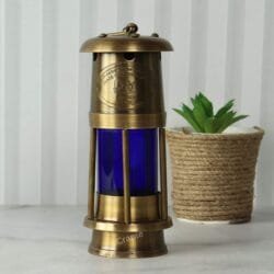 An antique brass mariner's lantern with a blue glass cylinder, displayed as a decorative item next to a small plant.