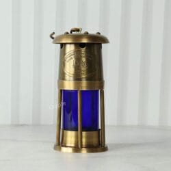 A straight-on front view of the brass and blue miner's style lantern on a white surface.