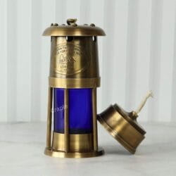 The removable brass oil burner leaning against the side of the blue lantern, showing the wick.
