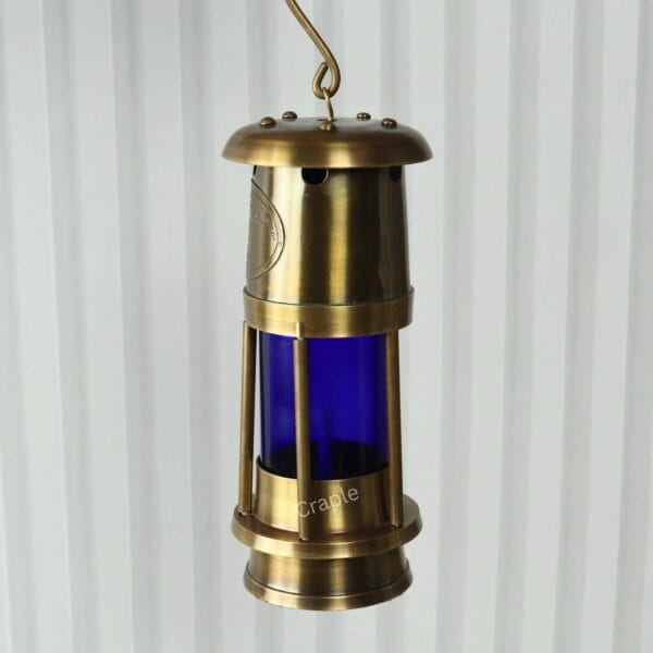 Brass Mariner’s Lantern-7 The antique brass lantern hanging by its metal hook against a striped background.