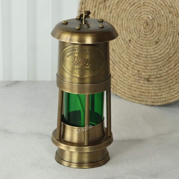 Brass Nautical Oil Lamp-1 Front view of a vintage brass nautical oil lamp with a green glass cylinder and a hook for hanging.