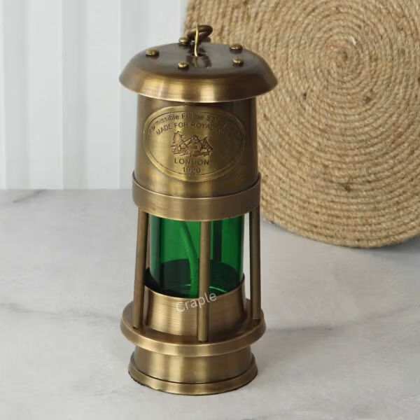 Front view of a vintage brass nautical oil lamp with a green glass cylinder and a hook for hanging.