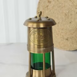 Angled view of the antique brass miner's style lantern, showing the details of the riveted top and protective cage.