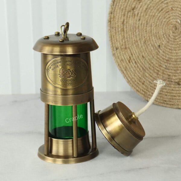 Brass Nautical Oil Lamp-4 The brass and green ship's lantern with the removable oil reservoir and wick placed beside the main body.
