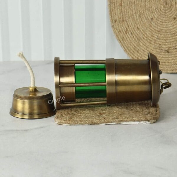 Brass Nautical Oil Lamp-6 The antique brass nautical lantern lying on its side with the oil burner and wick separated from the green lamp body.