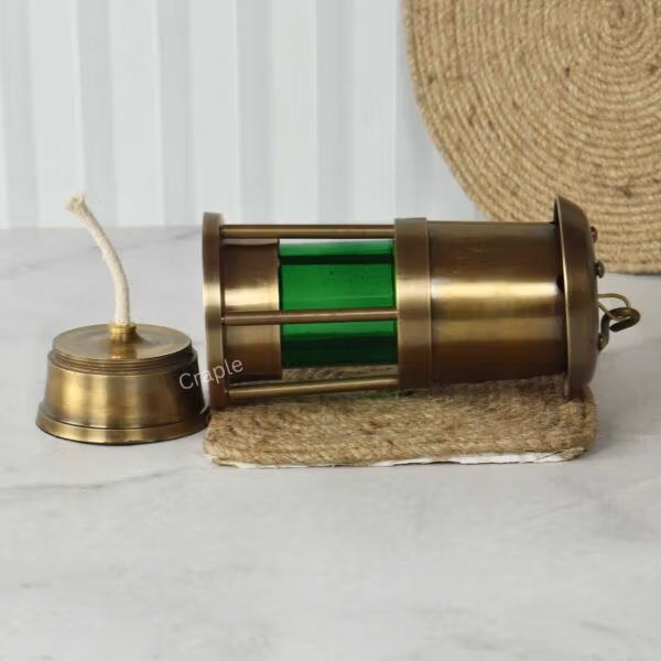 The antique brass nautical lantern lying on its side with the oil burner and wick separated from the green lamp body.