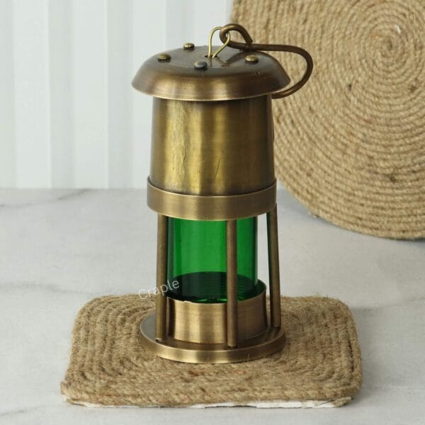 Brass Nautical Oil Lamp-7 The brass and green glass nautical oil lamp displayed upright on a rustic jute coaster.