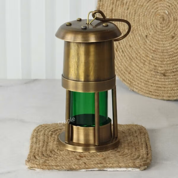 The brass and green glass nautical oil lamp displayed upright on a rustic jute coaster.