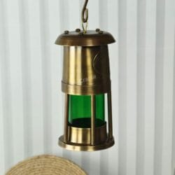 The brass nautical oil lantern hanging from its top hook, showcasing its use as a hanging light fixture.