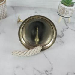 Top-down view looking into the brass ship's bell, showing the internal clapper and hand-knotted cotton lanyard.