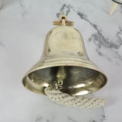 View from underneath the large brass nautical bell, highlighting its wide mouth and the internal ringing mechanism.
