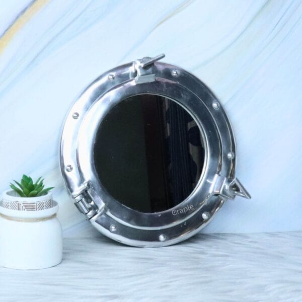 The nickel porthole mirror displayed as chic nautical wall decor in a room with a small plant.