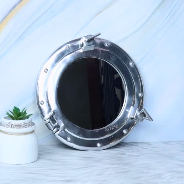 The nickel porthole mirror displayed as chic nautical wall decor in a room with a small plant.