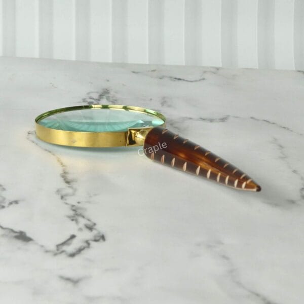 A vintage-style magnifying glass with a detailed, carved feather handle lying flat on a white marble tabletop.