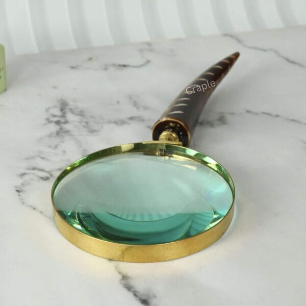 Close-up shot of the large 10cm magnifying lens, highlighting the shiny brass frame and clear 5X glass.