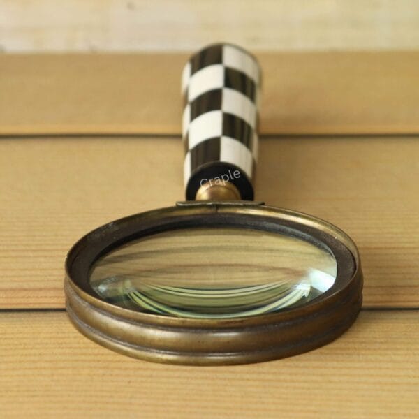Front-facing view of a decorative magnifier, highlighting the round 5X lens in an antique brass frame and the checkerboard handle.