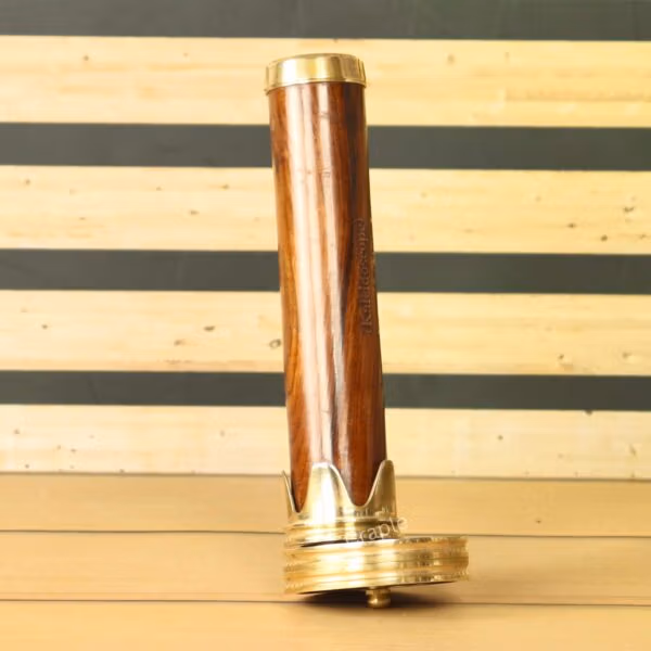 Full-length view of a vintage-style kaleidoscope with a wooden barrel and polished brass ends, standing upright on a table.