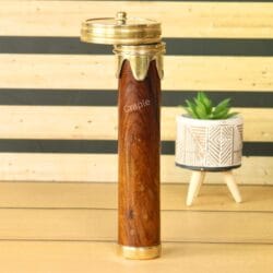 The wooden and brass kaleidoscope standing on a desk next to a small plant, showcasing it as a decorative item.