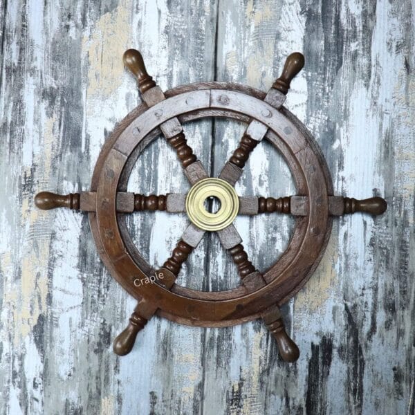 The decorative wooden ship's wheel mounted on a rustic, distressed wood wall, shown as nautical wall art.