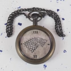 The Direwolf sigil pocket watch lying on a flat surface with its dark antique chain spread out above it.