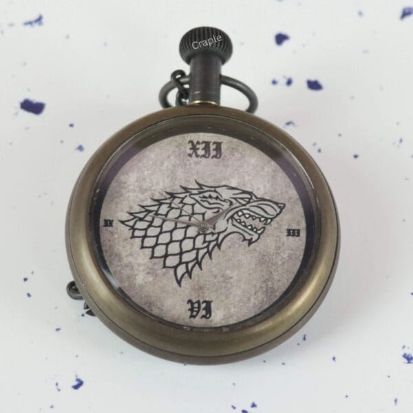 A close-up of the pocket watch dial, showing the detailed Direwolf sigil and vintage-style Roman numerals.